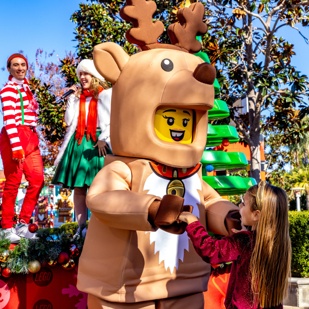 A child interacting with a LEGO reindeer character during a holiday celebration at LEGOLAND Resort, surrounded by festive decorations and performers